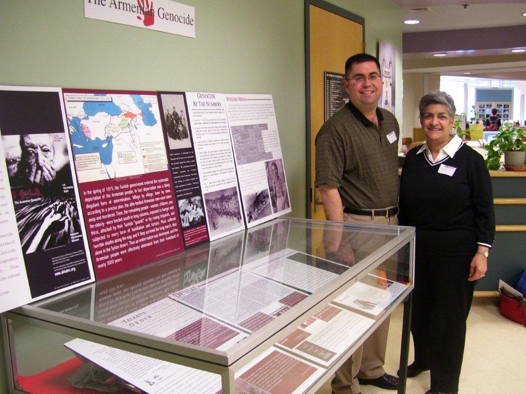 Sona Petrossian of the Newton Human Rights Commission is joined by Dro Kanayan, chairman of the Armenian Genocide Curriculum Committee of Merrimack Valley, at Newton South High School, where a compelling exhibit on genocide fills the library throughout April.