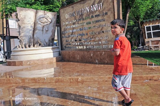 A Kurdish child walks past the memorial to the Armenian Genocide in Diyarbakir. The message on the memorial is written in several languages, including in Armenian, and states "We shared the pains so that they are not suffered again." Photo © 2014 Matthew Karanian, Reprinted with Permission.