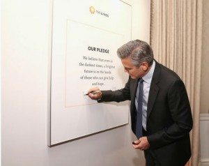 Clooney signs the 100 Lives pledge, which reads, "We believe that even in the darkest times, a brighter future is in the hands of those who can give help and hope."