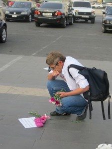 A passerby places flowers next to a pair of small, pink shoes