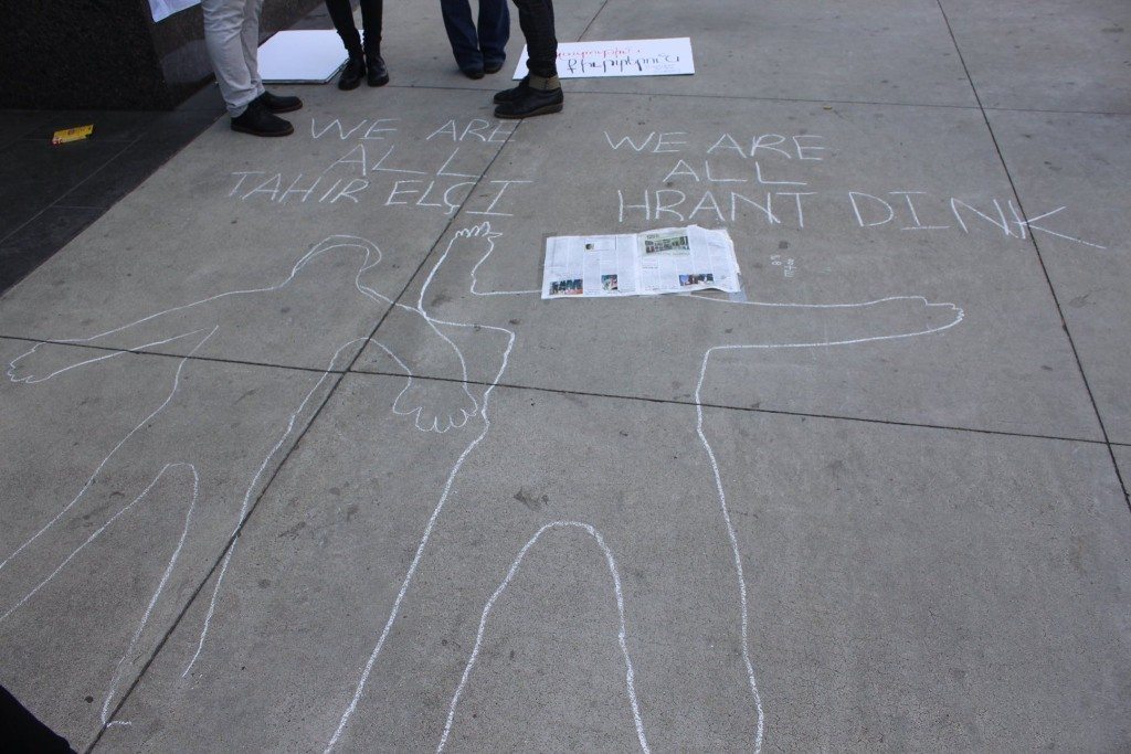 Chalk-outlines of human figures, symbolizing the bodies of Elçi and Dink, were drawn outside the Turkish Consulate’s front steps, turning the protest into a crime scene. 